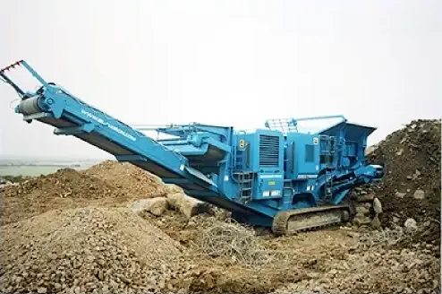 A blue tracked mobile crusher working on a heap of broken concrete and rubble