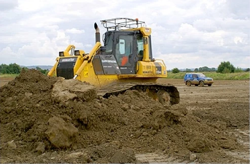 A yellow bulldozer pushing a heap of spoil across an open site