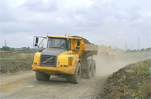 A yellow Volvo articulated dump truck on a dusty haul road, a second truck behind it