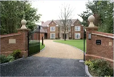 A large brick-built new home behind gated brick piers and a gravel drive
