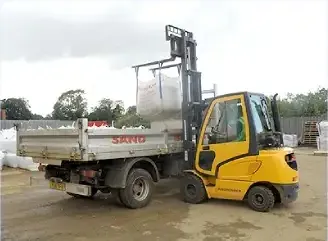 A yellow forklift lifting a bulk bag onto a tipper lorry