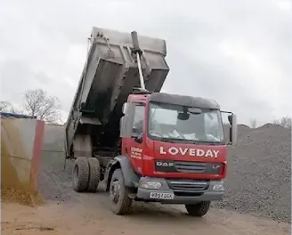 A red Loveday tipper lorry with its body raised beside aggregate stockpiles