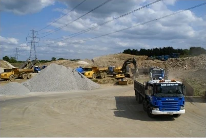A Clark tipper lorry crossing a quarry yard past aggregate stockpiles, yellow plant and pylons